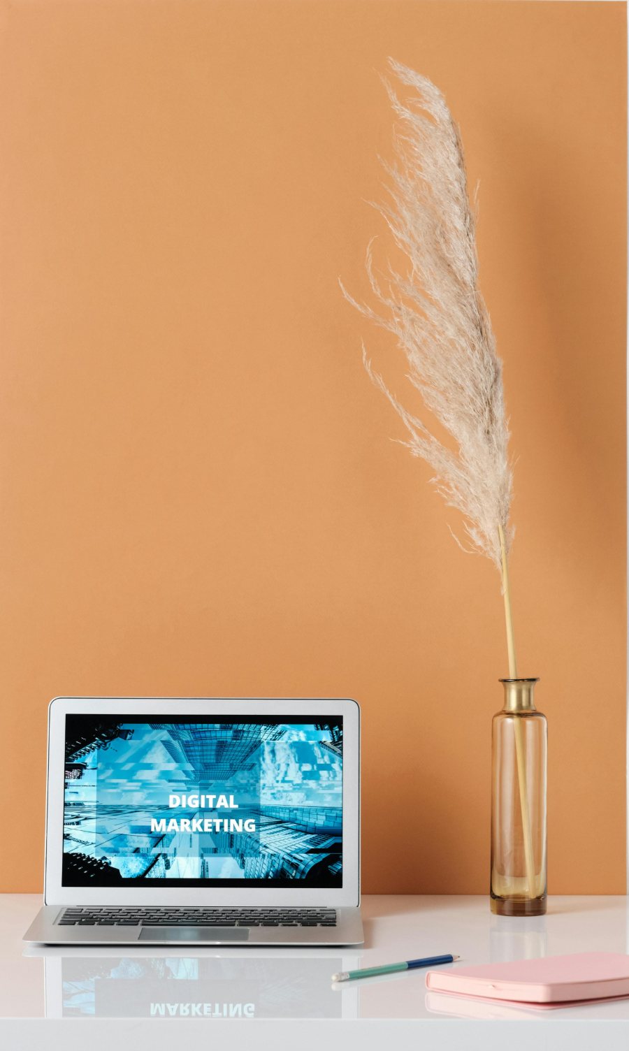 A digital marketing workspace laptop, notebook and pampas grass on a warm-toned desk